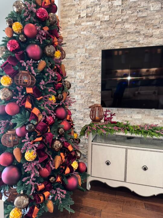Tree in burgundy velvet and copper ribbon beside a stone fireplace wall