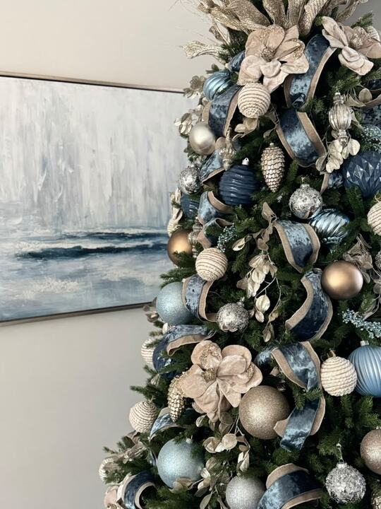 Tree in soft blue and champagne ornaments in front of an ocean painting